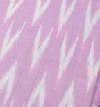 A hand holding a folded pink fabric with a white ikat pattern, with other patterned fabrics stacked underneath.